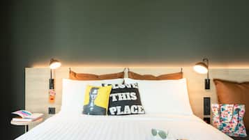 A neatly made bed with pillows, a bedside table with a book, and a wall-mounted lamp.