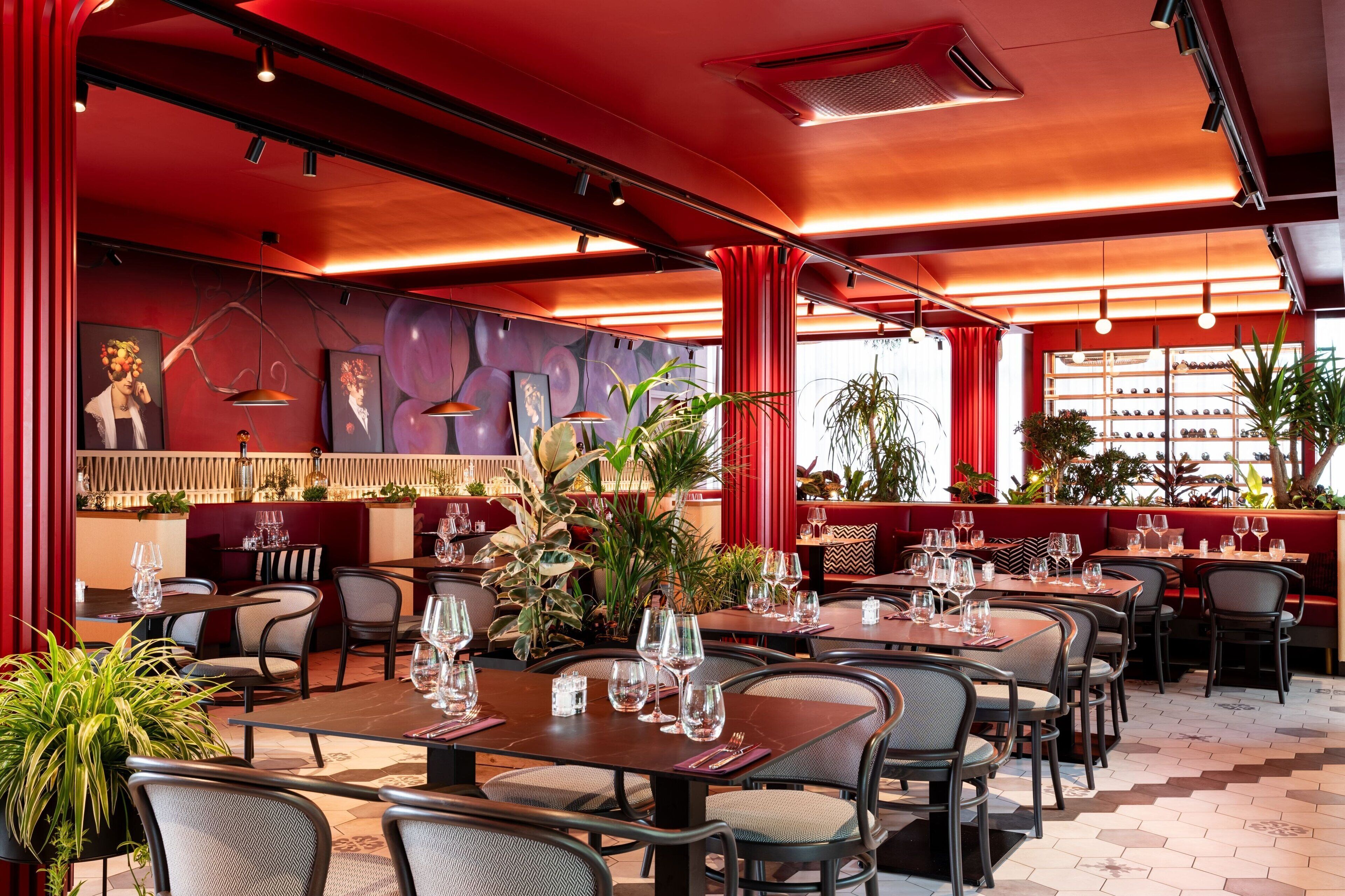 A restaurant with red walls, multiple dining tables, and chairs.