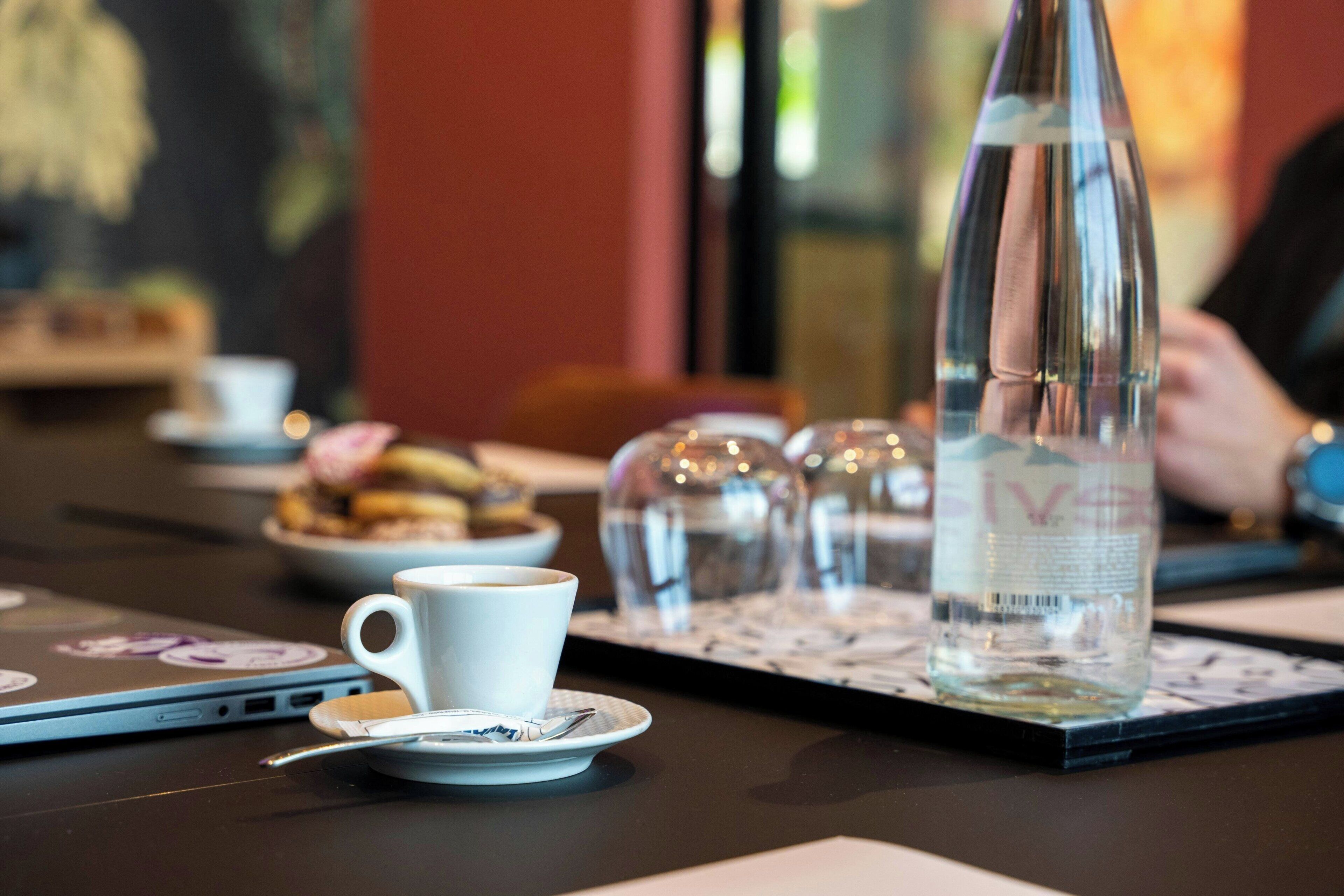 Une table avec une tasse blanche, une bouteille transparente et un ordinateur portable.