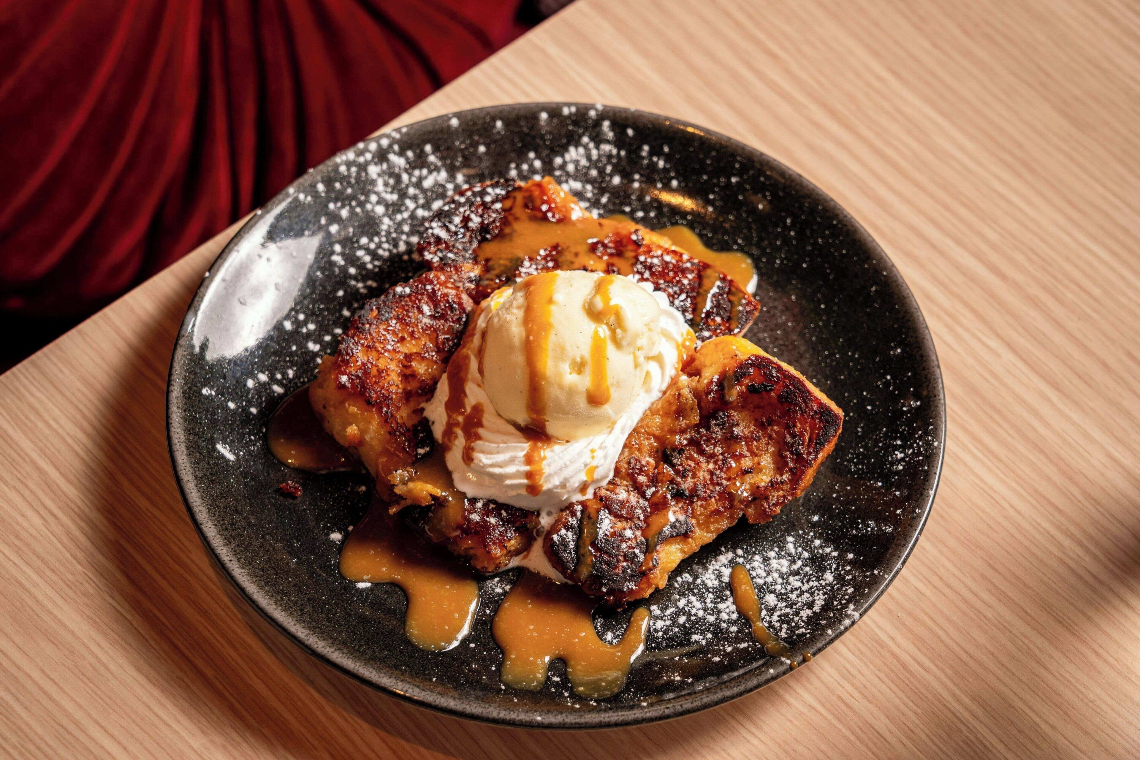 A dessert plate with a caramelized dessert, a scoop of ice cream, and a drizzle of caramel sauce.