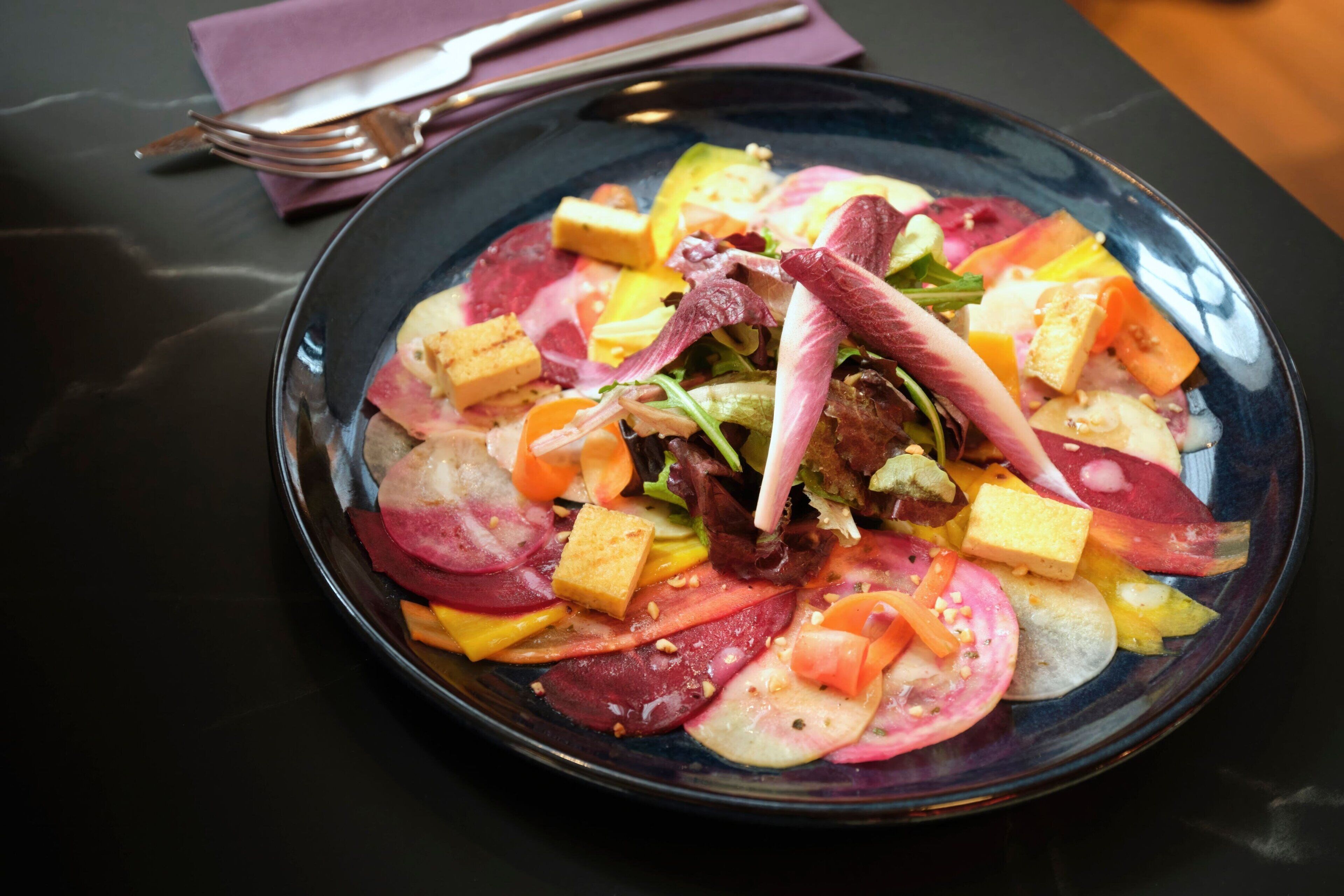 A plate of colorful salad with various vegetables and tofu cubes.