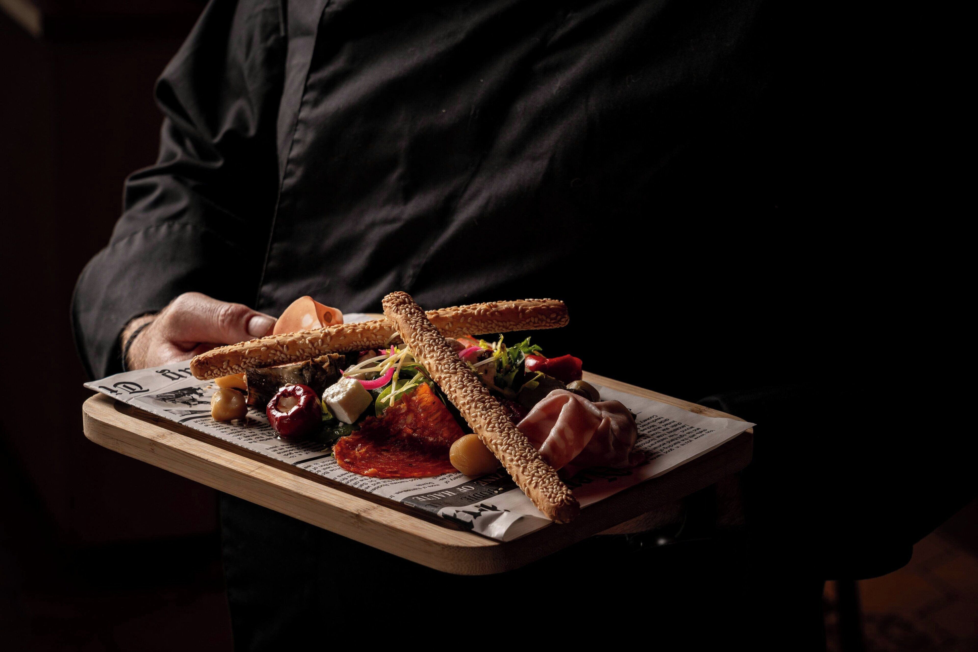 A person holding a tray with various food items including bread, cheese, and vegetables.
