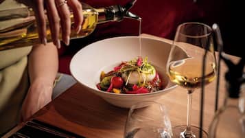 A person pouring a clear liquid into a white bowl containing a food dish, with a wine glass beside it.