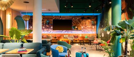 A modern lounge area with seating, a large TV screen, and decorative plants.