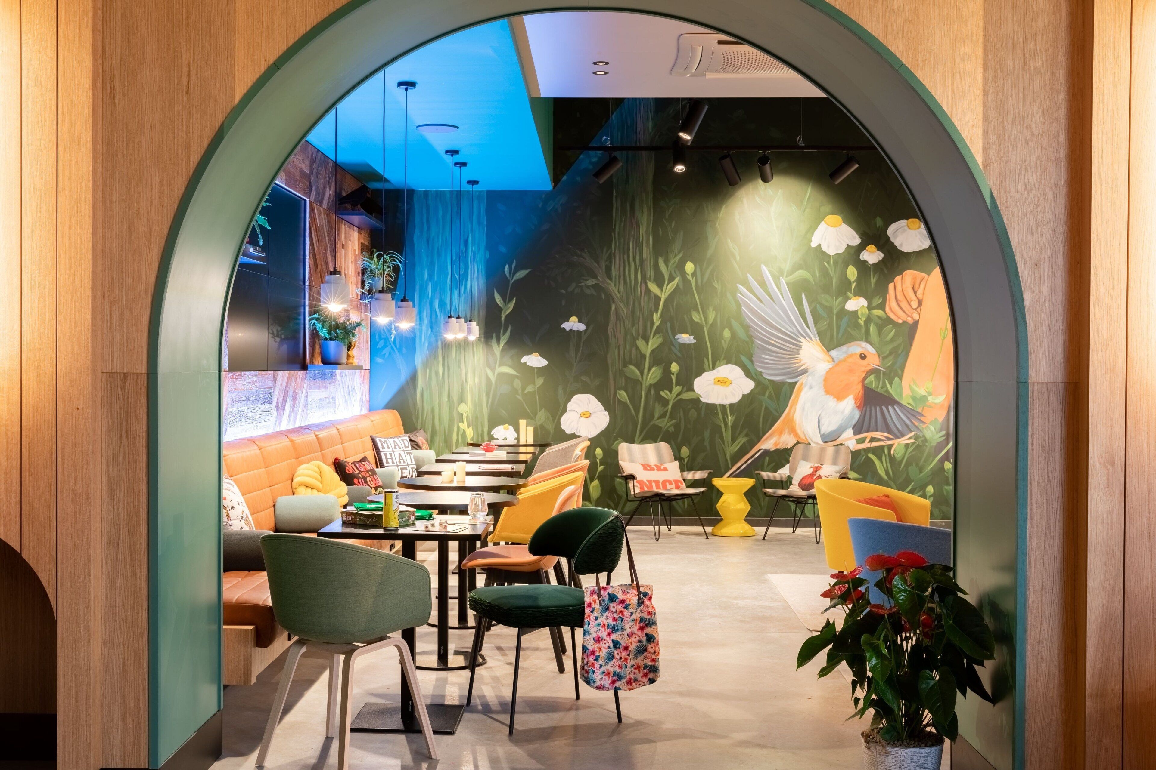 Un interior acogedor con un arco de madera, una zona de comedor con sillas y mesas, y un mural de pájaros y flores en la pared.