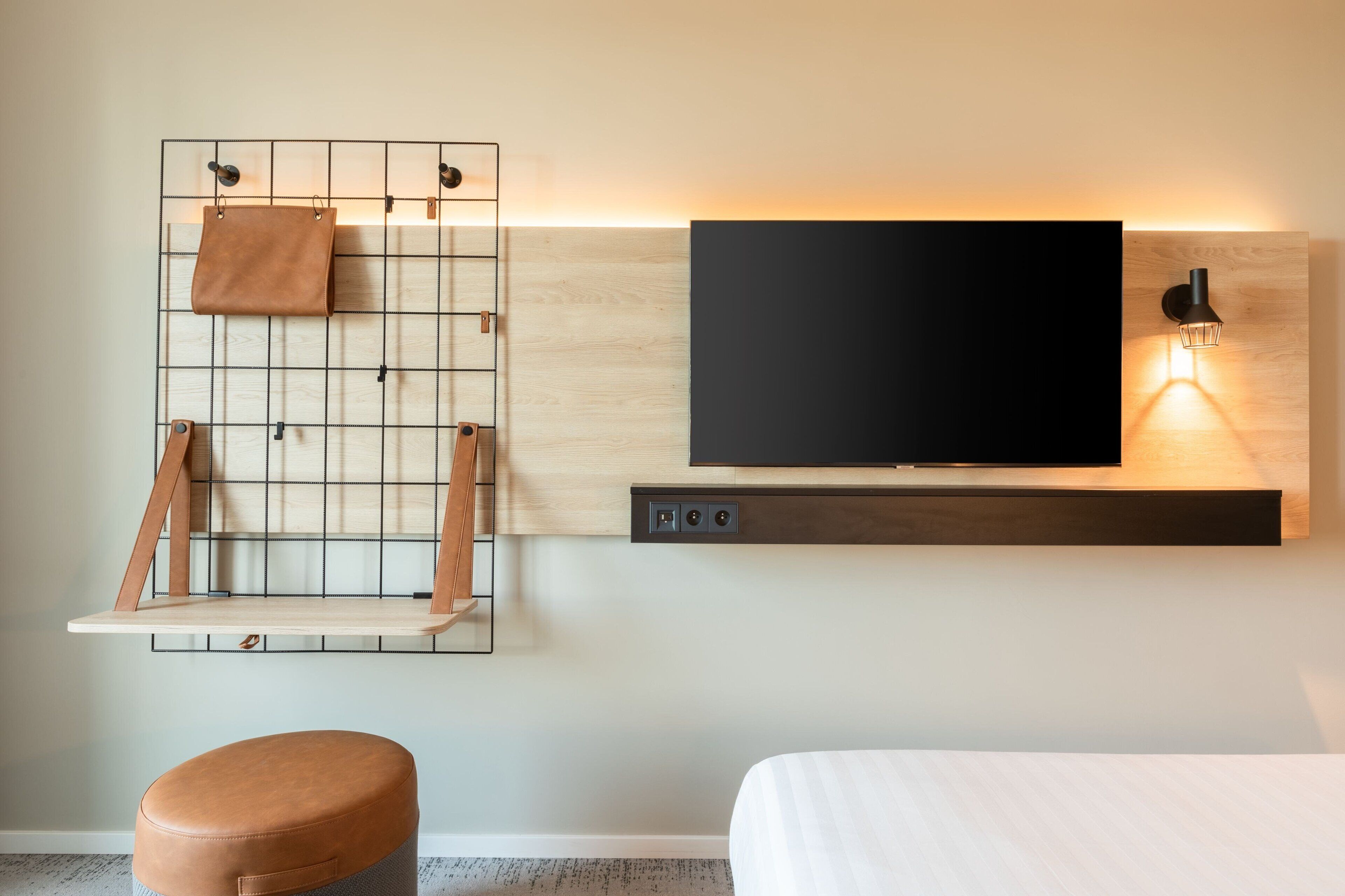 Una habitación moderna con televisor montado, una estantería de madera con un bolso de cuero y una lámpara de pared.