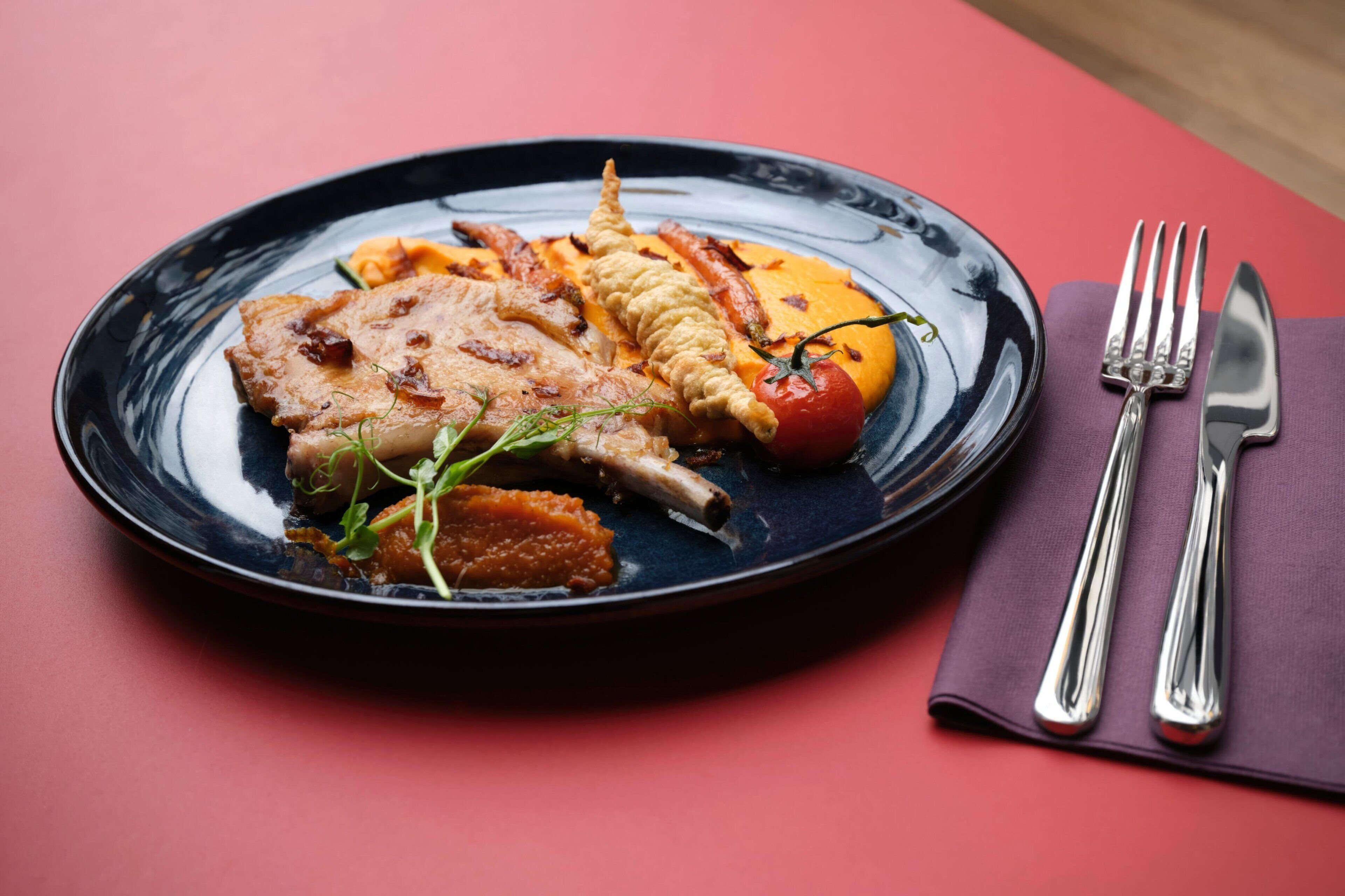Un plato de comida sobre una mesa, con un tenedor y un cuchillo sobre una servilleta.