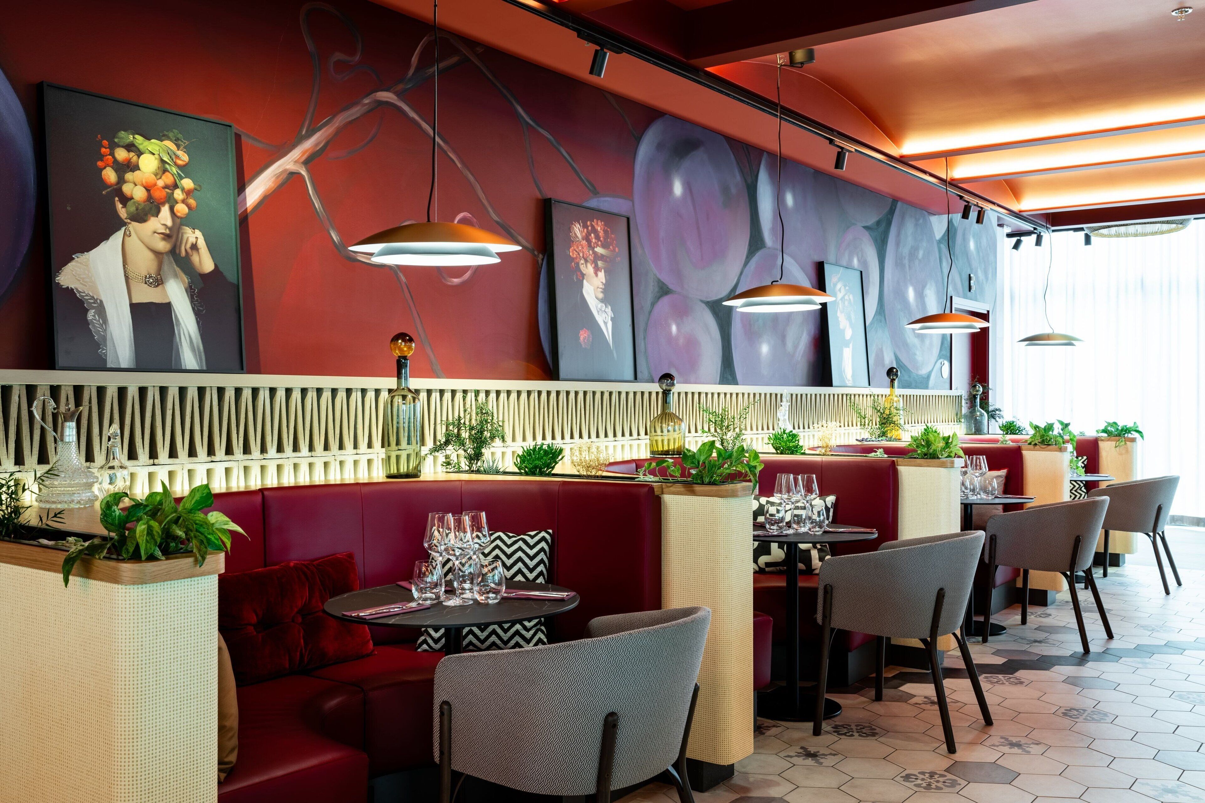 A restaurant interior with red booths, round tables, and modern pendant lighting.