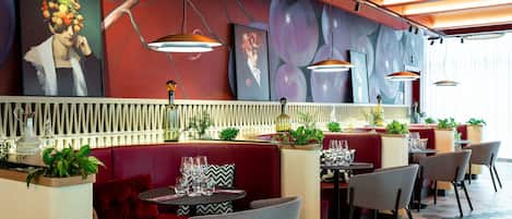 A restaurant interior with red booths, round tables, and modern pendant lighting.