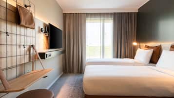 A hotel room with a bed, a TV, a desk with a chair, and a window with curtains.