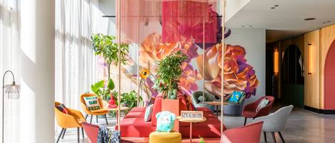 A modern lounge area with colorful seating, plants, and a vibrant floral mural.