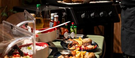 A buffet table with various dishes, a grill in the background, and condiments.