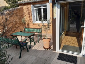 Un espace extérieur aménagé avec une table et des chaises, un pot de fleurs et une fenêtre dotée d’un thermomètre.