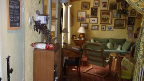 A cozy room with a wooden desk, a green sofa, and a dining area. There are framed pictures on the walls and a chalkboard menu on the wall. - Atypical house 15 minutes from Carcassonne (PEZENS)