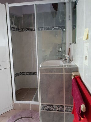 Une salle de bain avec une douche à parois de verre, un lavabo avec un miroir et une serviette rouge suspendue à un porte-serviettes blanc.