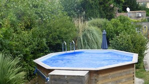 A rectangular hot tub with a wooden exterior, surrounded by lush greenery and a stone wall. - Atypical house 15 minutes from Carcassonne (PEZENS)