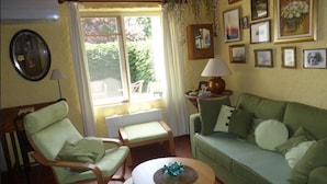 A living room with a green sofa, a rocking chair, a small table with a decorative item, and a window with curtains. - Atypical house 15 minutes from Carcassonne (PEZENS)