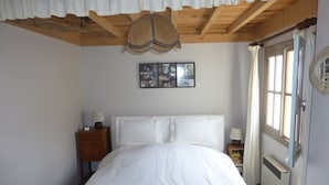 A bedroom with a wooden ceiling, a bed with white linens, a nightstand with a lamp, and a window with curtains. - Atypical house 15 minutes from Carcassonne (PEZENS)