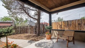 Un porche cubierto con una silla de madera, una planta en maceta y un pequeño árbol.