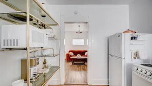 Una cocina compacta con electrodomésticos blancos, un sofá rojo al fondo y piso de madera.