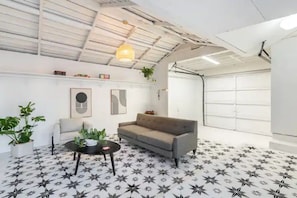Relax in this spacious living area with a high ceiling, featuring a sofa, coffee table, and lush greenery.