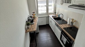 A compact kitchen with white cabinets, a wooden countertop, a black stove, and a window providing natural light. - Cozy apartment in the center (Chemnitz)