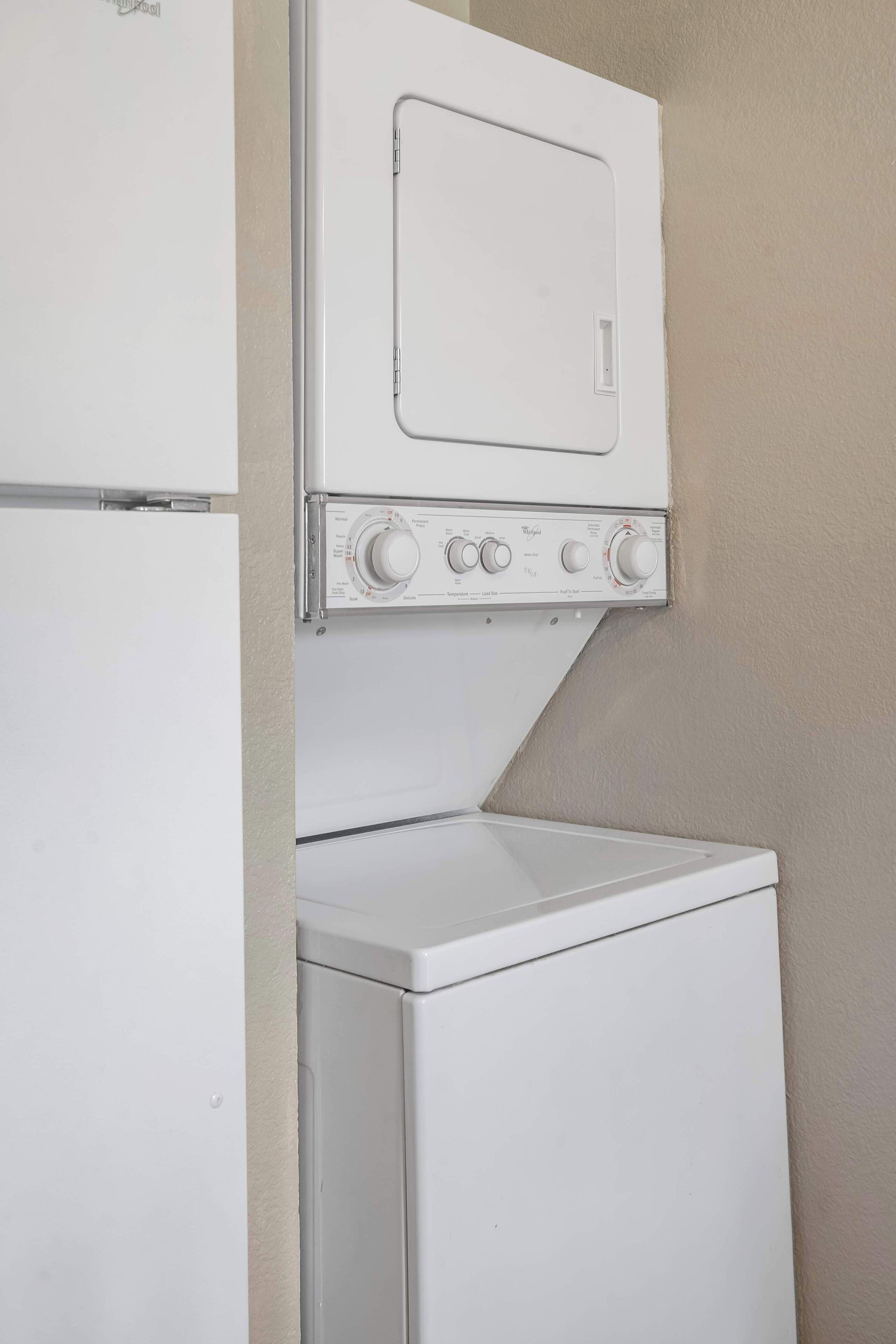 Un lavadero pequeño y funcional con lavadora y secadora apiladas, un panel de control y una ventana.