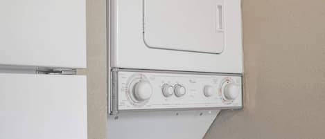 Un lavadero pequeño y funcional con lavadora y secadora apiladas, un panel de control y una ventana.