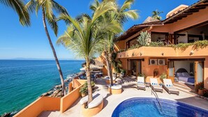 Une propriété située en bord de mer, dotée d’une piscine, de chaises longues et de palmiers.