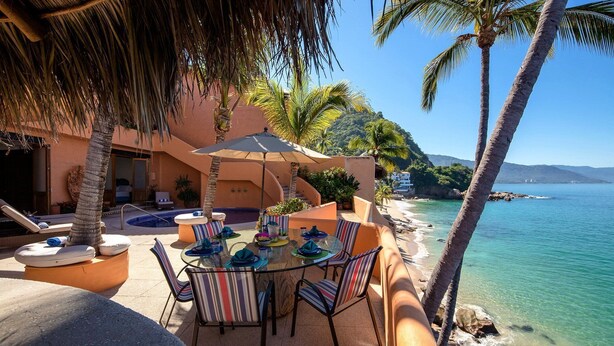 Une terrasse donnant sur la plage, avec une table en verre, des chaises à rayures et un espace piscine.
