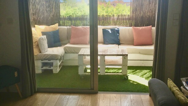A room with a sliding glass door leading to an outdoor area with a wooden deck, a white sofa with cushions, and a small table. - Grand Studio Avec Terrasse et vue mer (Saint-Laurent-du-Var)
