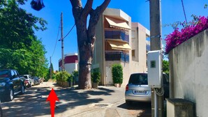 A narrow street with parked cars, a large tree, and a building with balconies. - Grand Studio Avec Terrasse et vue mer (Saint-Laurent-du-Var)