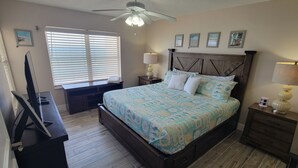 Un dormitorio con cama de madera, un escritorio, un televisor y un ventilador de techo.