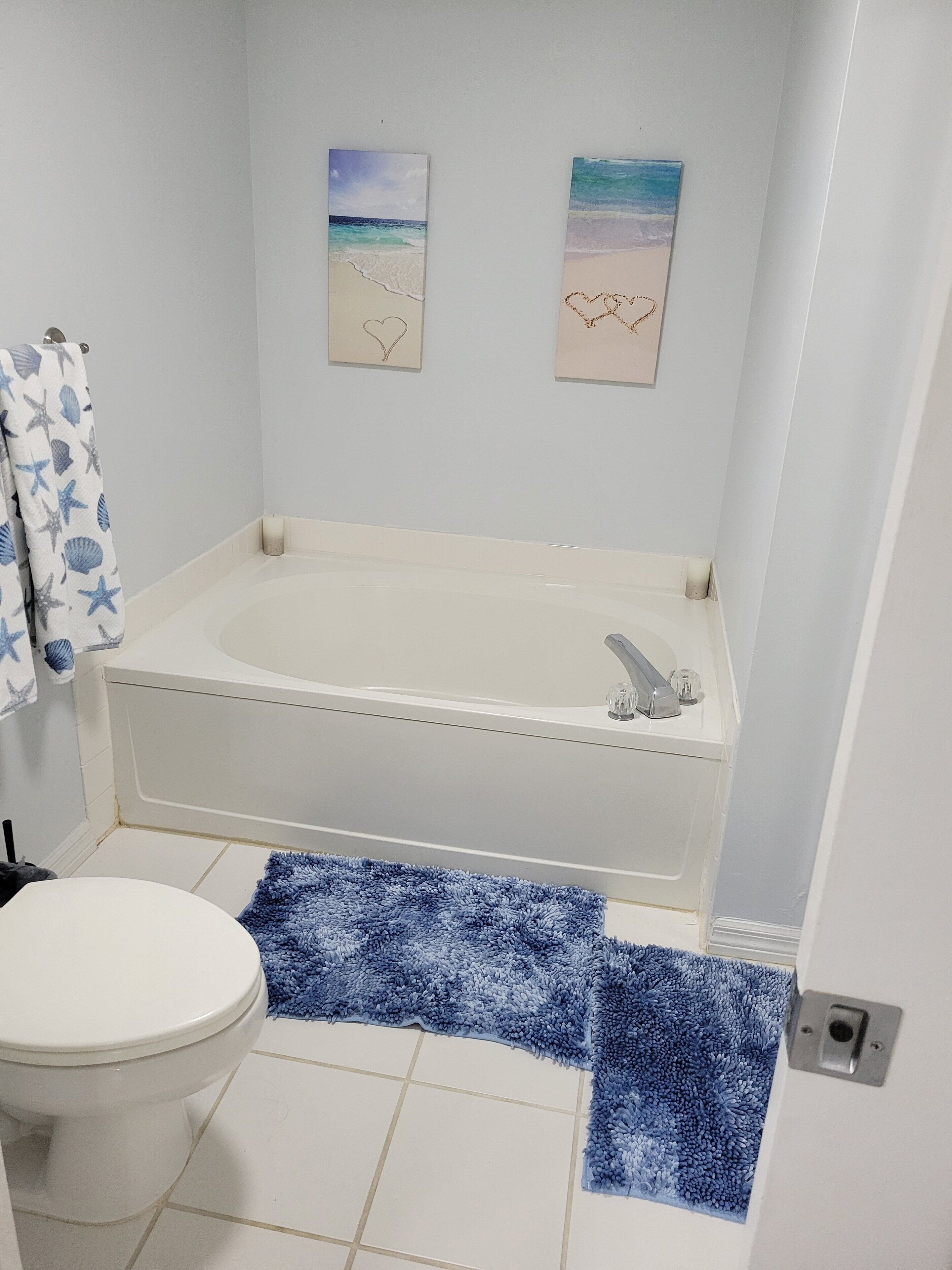 A bathroom with a bathtub, toilet, and a blue rug.