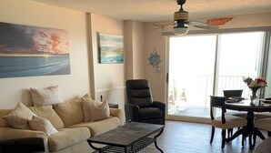 Una sala de estar con un sofá, un sillón, una mesa de centro y una mesa de comedor con sillas.