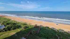 Una playa con un paseo marítimo de madera que conduce a la orilla, rodeada de vegetación.