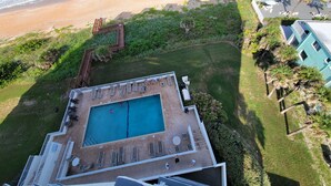Vista aérea de un complejo turístico con piscina, acceso a la playa y abundante vegetación.