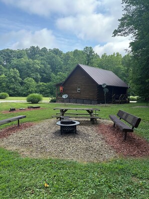 A rustic wooden cabin with a picnic table and benches in a grassy area surrounded by trees. - Welcome to our peaceful, rustic cabin in the Hocking Hills Area (Wellston)