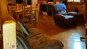 A cozy cabin interior with a wooden ceiling, a dining area, a living room with a leather sofa, and a kitchen with modern appliances. - Welcome to our peaceful, rustic cabin in the Hocking Hills Area (Wellston)
