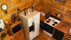 A compact wooden cabin with a dining table, chairs, a refrigerator, a stove, and a microwave. - Welcome to our peaceful, rustic cabin in the Hocking Hills Area (Wellston)