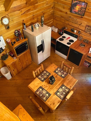 Una cabaña de madera compacta con una mesa, sillas, un refrigerador, estufa y microondas.