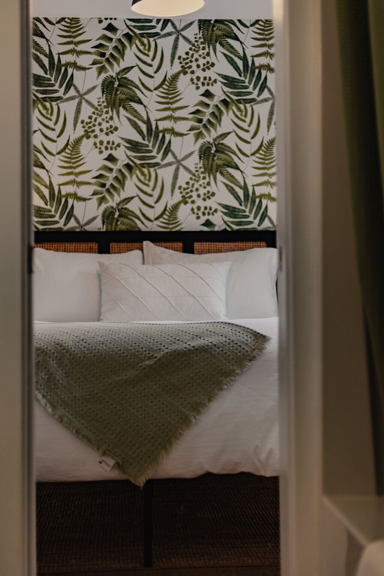 Ein Hotelzimmer mit Bett, Kissen, Decke und einer Wand mit Blattmuster.