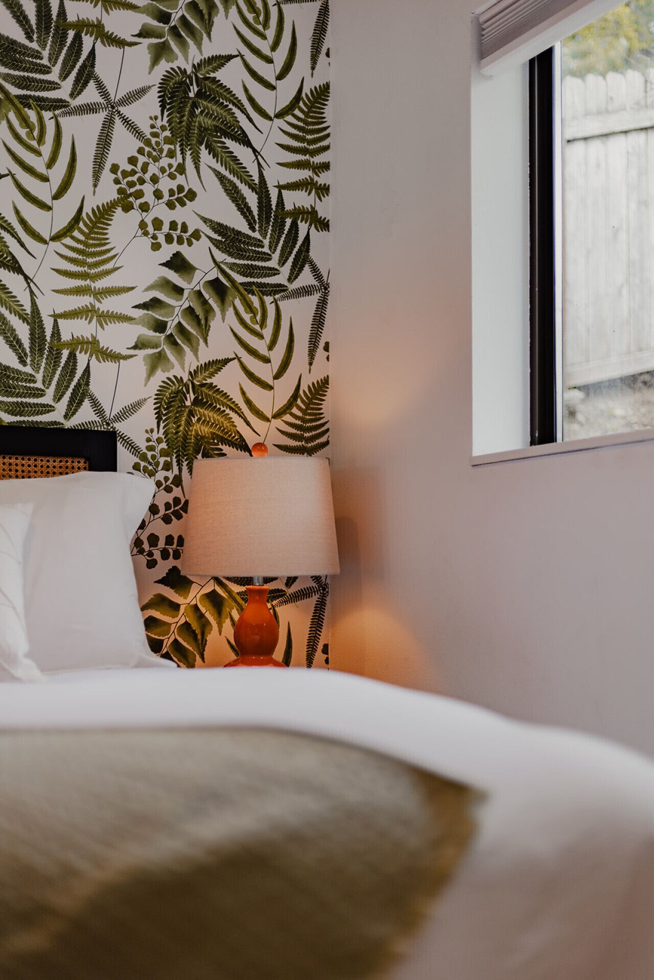 Een hotelkamer met een bed, een nachtkastje met een lamp en een muur met een bladeren patroon.