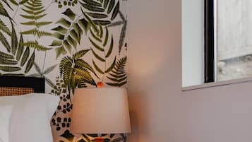 Een hotelkamer met een bed, een nachtkastje met een lamp en een muur met een bladeren patroon.