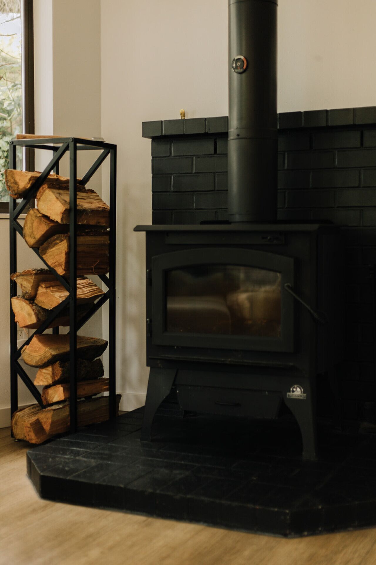 Ein Kaminofen mit schwarzem Backsteinrahmen und einem Metallregal für Holzscheite.