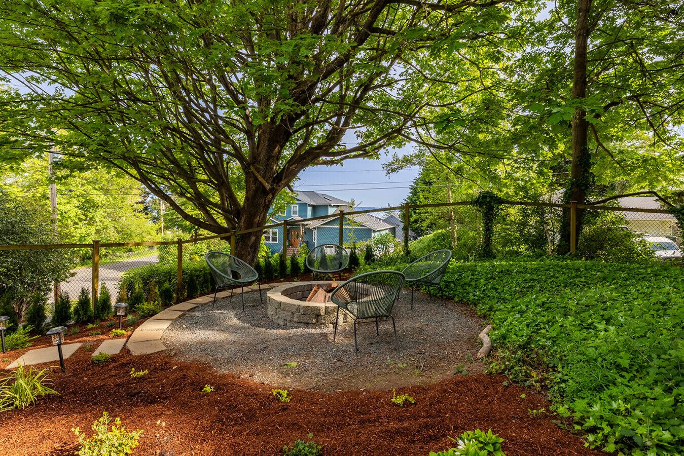 A circular outdoor seating area with a fire pit, surrounded by a gravel path and greenery.