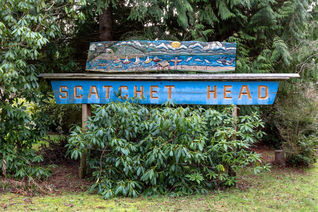 Un letrero con el texto 'SCATCHET HEAD' y un mural pintado que muestra un paisaje marino con barcos y una ballena.