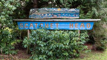 Un letrero con el texto 'SCATCHET HEAD' y un mural pintado que muestra un paisaje marino con barcos y una ballena.