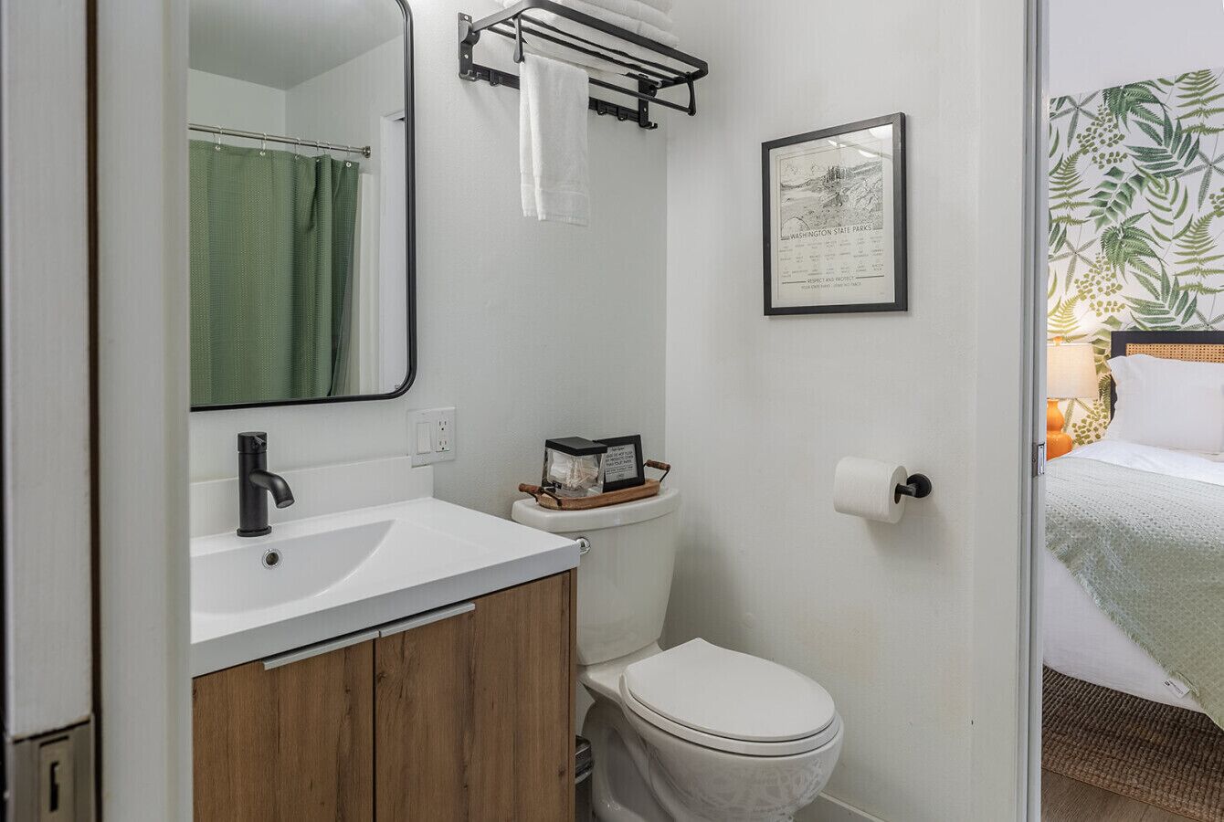 A bathroom with a white sink, a toilet, and a mirror. There is a towel rack above the sink and a framed picture on the wall.
