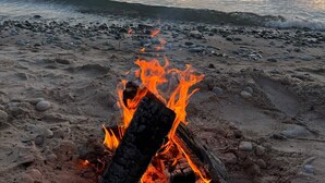 A beach scene with a fire on the sand, a calm sea, and a sunset in the background.